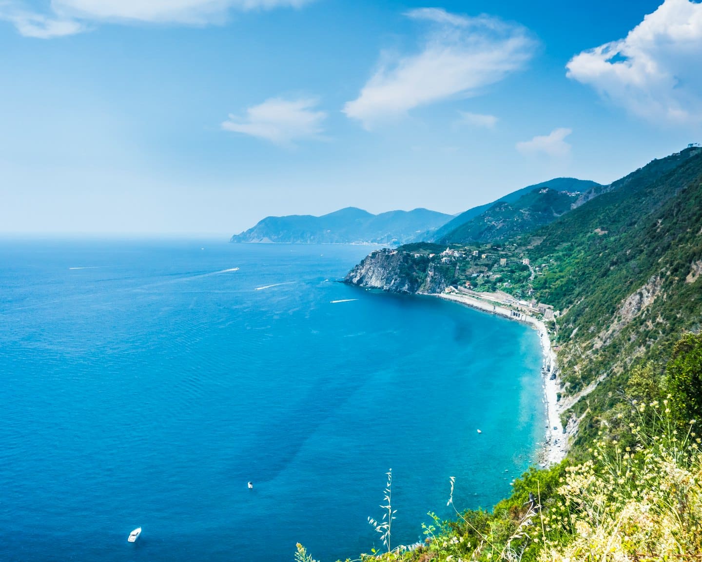 Costa mediterranea con colline verdi, scogliere e mare turchese.